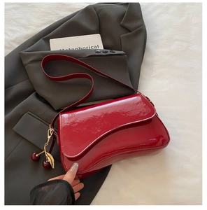 Detail of red patent leather shoulder bag with cherry charm on grey blazer