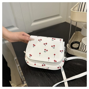 Detail of white saddle bag with red cherry print and slender shoulder strap