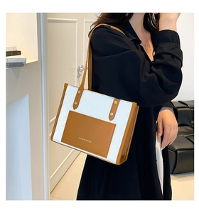 Detail shot of bicolor tote bag with gold lettering shown on a model's shoulder