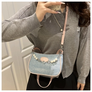 Blue denim crossbody bag with pink leather trim and pearl chain strap worn by model
