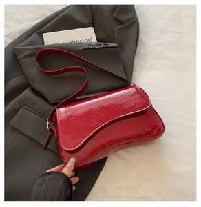 Chic red patent leather underarm bag with asymmetric flap shown on a blazer and linens