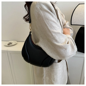 Detail of black puffy half-moon shoulder bag with gold hardware and quilted texture