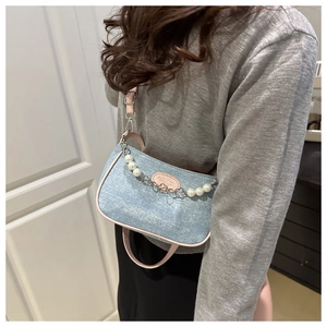 Detail view of light blue denim crossbody bag with pink trim and decorative pearl chain