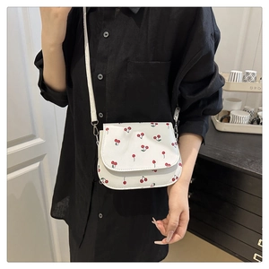 Close-up of white cherry print saddle bag featuring silver hardware and synthetic leather finish