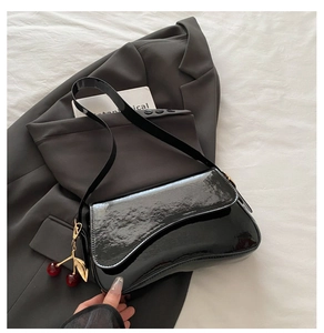 Close-up of black patent leather underarm bag with a cherry pendant on a grey blazer