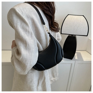 Detail of a black crescent underarm bag with textured pleats worn by a model in a minimal room