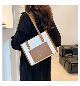 Detail of woven white tote bag with brown leather pocket and gold rivet handles on model