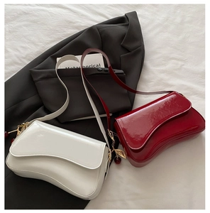 Detail of patent leather underarm bags with wavy flap design and cherry pendant charms