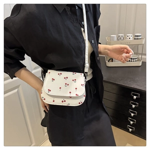 Close-up of white crossbody bag with red cherry prints and silver chain details