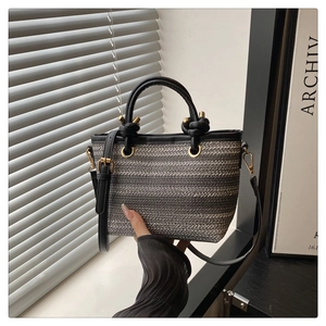 Détail du sac seau en paille ethnique avec rayures grises et poignée en cuir noir