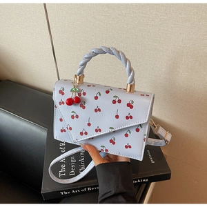Detail of light blue cherry print handbag with braided handle and cute fruit pendant