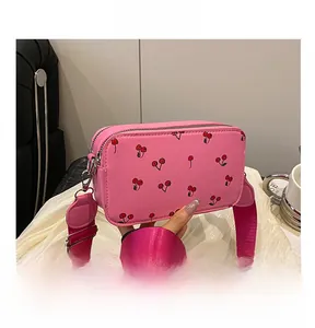 Detail view of pink crossbody bag with cherry prints and a wide fabric shoulder strap