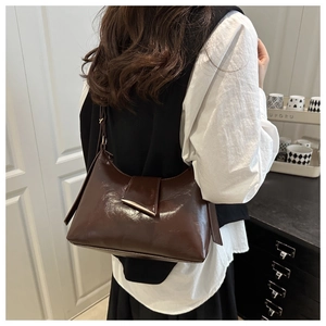 Detail of dark brown glossy leather crossbody bag featuring a gold triangle hardware clasp