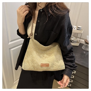 Dettaglio della borsa a spalla in paglia beige con etichetta in pelle e trama intrecciata