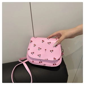 Detailed close-up of cherry pattern on small pink saddle bag with silver hardware