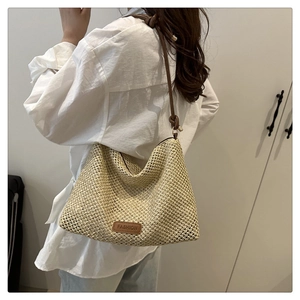Dettaglio della borsa a tracolla in paglia intrecciata con patch in pelle e tracolla fine