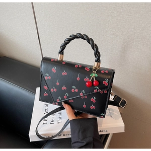 Detail of black PU leather handbag featuring cherry prints and a cute cherry-shaped pendant