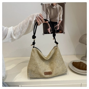 Dettaglio borsa tote in paglia intrecciata con manici in corda nera e logo in pelle