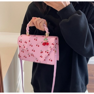 Detailed view of pink cherry print handbag with twisted handle and charm on black outfit