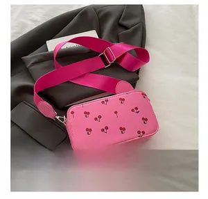 Detail of pink crossbody bag with cherry prints and wide fabric strap on a blazer