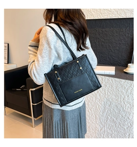 Rear view of a model wearing a black woven leather tote bag with a golden brand logo