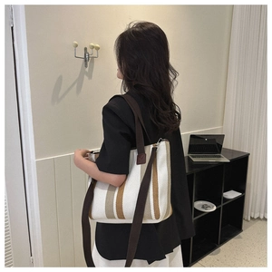 Close-up of striped canvas tote bag featuring premium leather trim and wide fabric strap