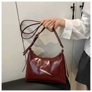 Detail of burgundy glossy leather underarm bag with gold triangle clasp and shoulder strap