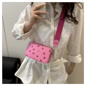 Detailed shot of pink crossbody bag with cherry prints and a wide fabric strap