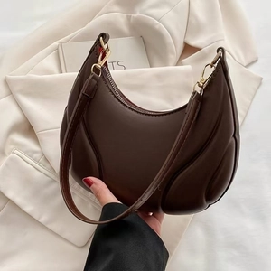 Brown half-moon underarm bag with pleated texture and golden hardware in lifestyle setting