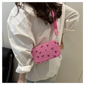 Detail of pink saddle bag with cherry pattern and wide strap on white shirt