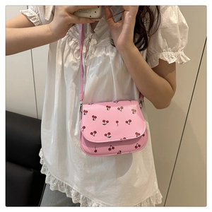 Model wearing a pink crossbody bag with cherry prints and a sleek chain strap