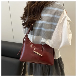Detail of burgundy patent leather shoulder bag with gold hardware worn by model