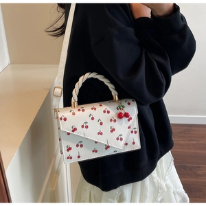 Detail of white cherry print handbag featuring twisted handle and red cherry charm decoration