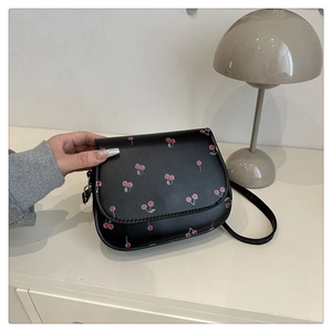 Close-up of black PU leather saddle bag with red cherry print on a white table