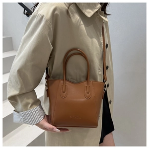 Brown leather bucket bag styled with a model against a minimalist white staircase background
