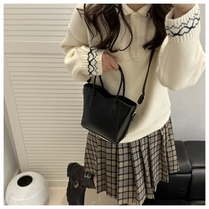 Lifestyle view of a black minimalist bucket bag styled with a plaid skirt and white top