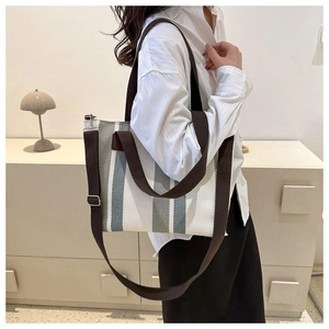 Detail of blue striped canvas tote with brown straps and metal buckle on side