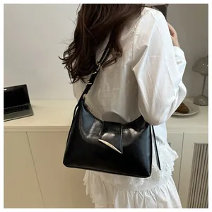 Close-up of black glossy leather crescent bag with gold buckle on model shoulder