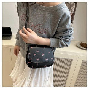 Detail of a black leather saddle bag with cherry print worn by a model in casual outfit