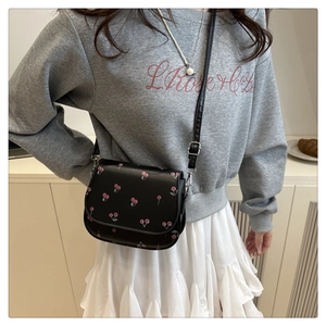 Detail shot of black leather saddle bag with cherry print and delicate chain strap