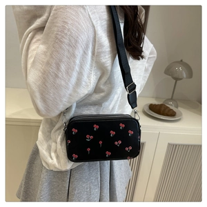 Detail showing a black saddle bag with cherry prints and a wide woven strap on a model