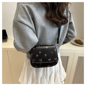 Close-up of black cherry print saddle bag with slim strap worn by a model in daily life