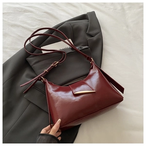 Detailed view of dark red saddle bag featuring elegant gold metal clasp on fabric