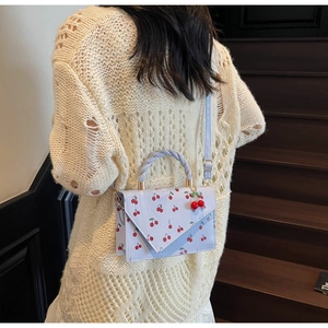 Detail of light blue cherry print handbag showing the woven handle and 3D cherry charm