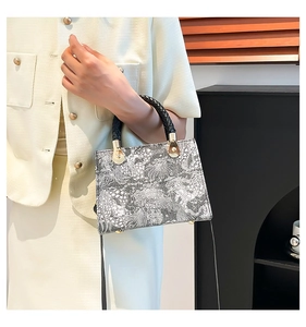 Detailansicht der grauen Print-Handtasche mit schwarzen Webgriffen und Gold-Beschlägen