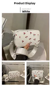 Detail of white camera bag featuring red cherry prints and adjustable wide shoulder strap