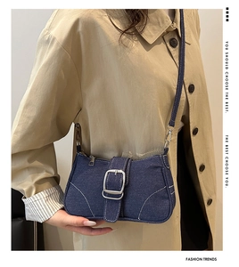 Detailed close-up of dark denim shoulder bag with silver buckle and contrast stitching