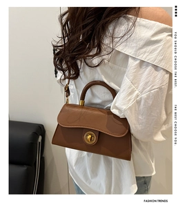 Detail einer braunen Ledertasche mit goldener Rundschnalle und verstellbarem Trageriemen