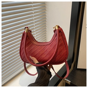 Detail of deep red woven crescent bag with gold metal accents and shoulder strap