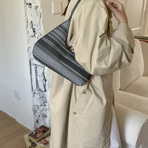 Detail of a half-moon woven hobo bag in grey tweed worn with a beige trench coat